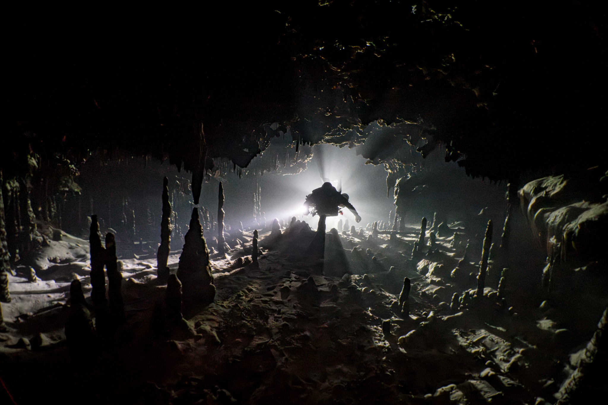 Cave diver silhouetted against beams of light inside a decorated underwater cave